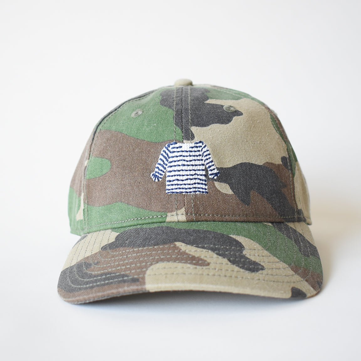 The Sara Fitz Striped Shirt Hat, Camo, is a cotton baseball cap with camo print, featuring a blue and white striped sweater embroidered on the front and an adjustable back strap. Shown on a plain white background.