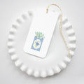 A white ruffled plate holds a Sara Fitz Blueberry Tea Tin Tag featuring a succulent illustration. The handy rectangular tag hangs by yellow and white baker's twine, making it charming for any occasion.